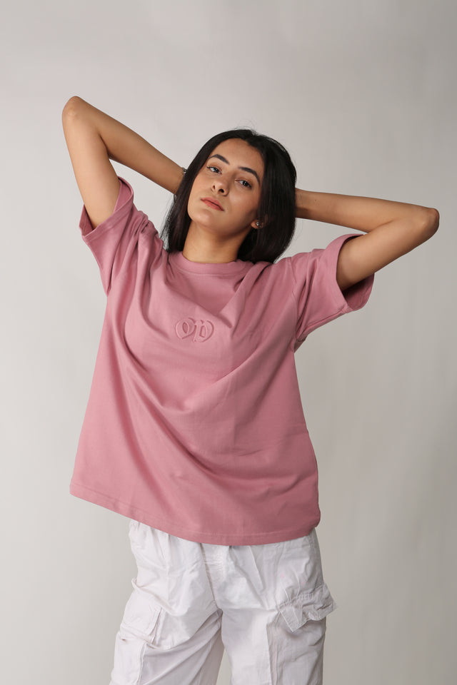 Female model styled in EMBOSSED LOGO T-shirt – oversized pink streetwear tee with tactile 3D embossed logo, paired with accessories and bold expression