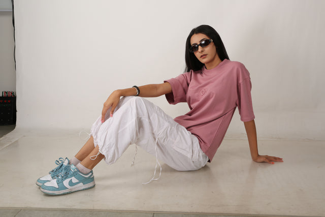 Female model styled in EMBOSSED LOGO T-shirt – oversized pink streetwear tee with tactile 3D embossed logo, paired with accessories and bold expression