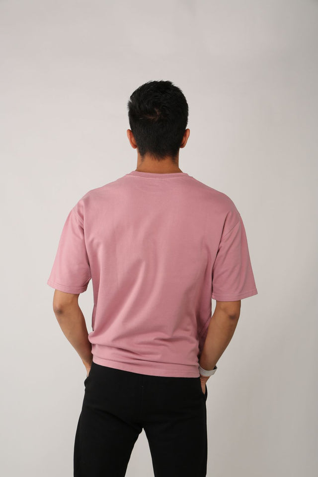 Back view of male model in EMBOSSED LOGO T-shirt – soft pink oversized fit with drop shoulders and minimalist streetwear vibe