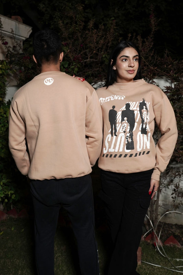 Couple wearing matching beige Guts & Glory sweatshirts by Outdrip, showing off the unisex design and bold print.
